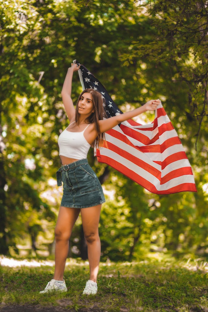 A woman joyfully displays the American flag in a sunny park.
