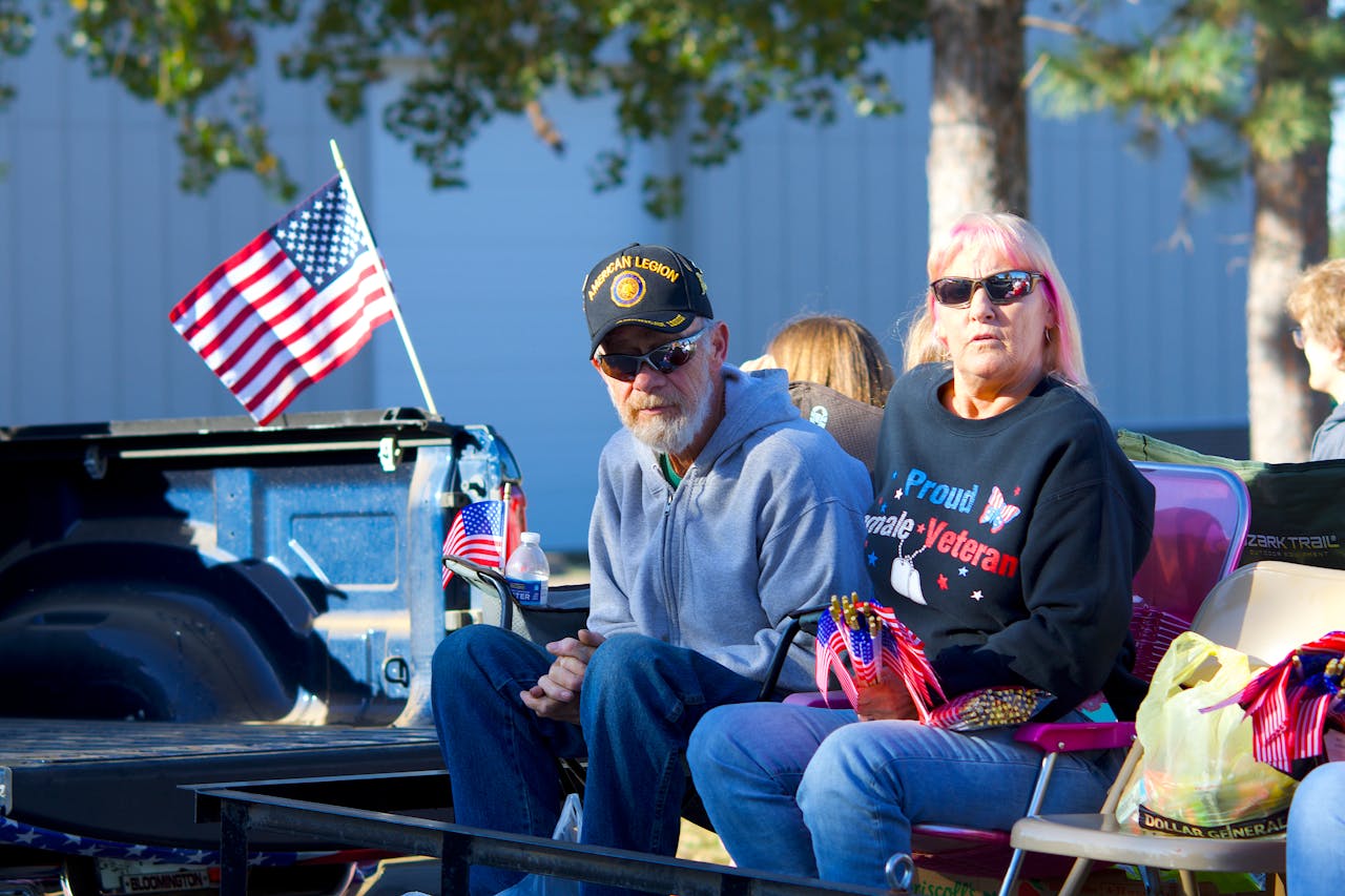 Senior veteran couple in a parade setting with American flags, showcasing patriotism and community spirit.